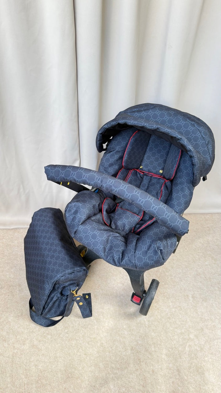 Black monogram Doona+ car seat cover set with red piping, matching padded footmuff and separate canopy cover, installed on Doona+ stroller frame, front view.