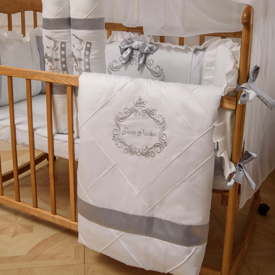 Baby crib with white and gray bedding set featuring a decorative emblem.