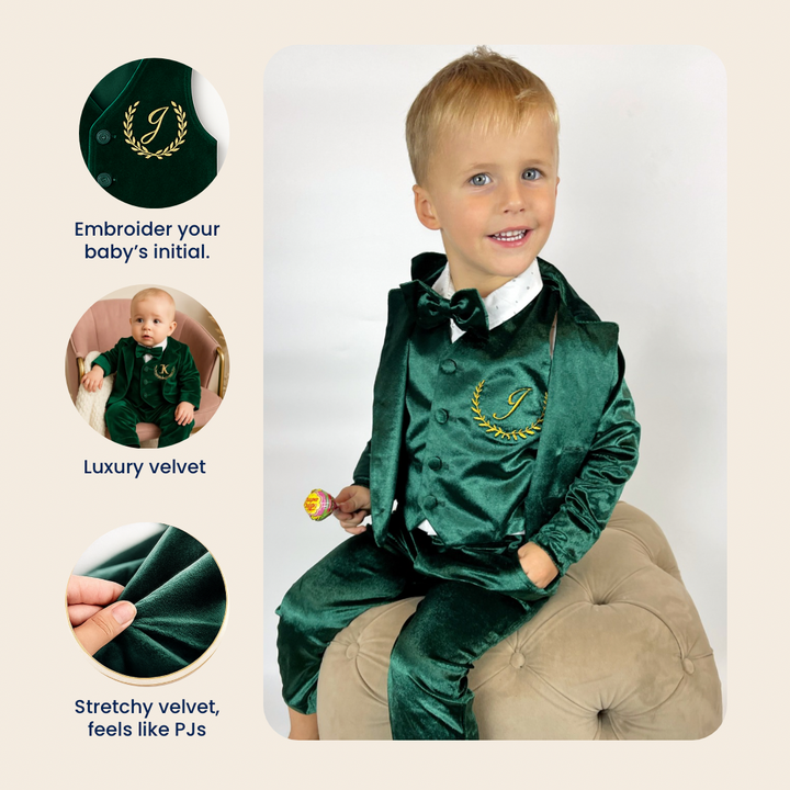 Child wearing a green velvet suit with embroidered initial, sitting on a cushion.