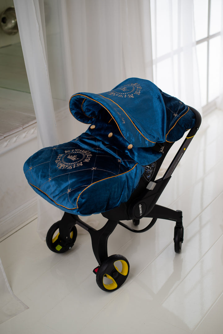 Luxury blue velour baby car seat cover set with gold embroidery details and gold piping, installed on a Doona car seat and photographed in a bright, minimal interior.