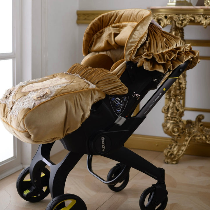 Luxury gold velvet baby car seat cover set installed on a car seat, featuring a quilted canopy, soft footmuff with delicate lace details and pink embroidery, photographed in an elegant interior setting.