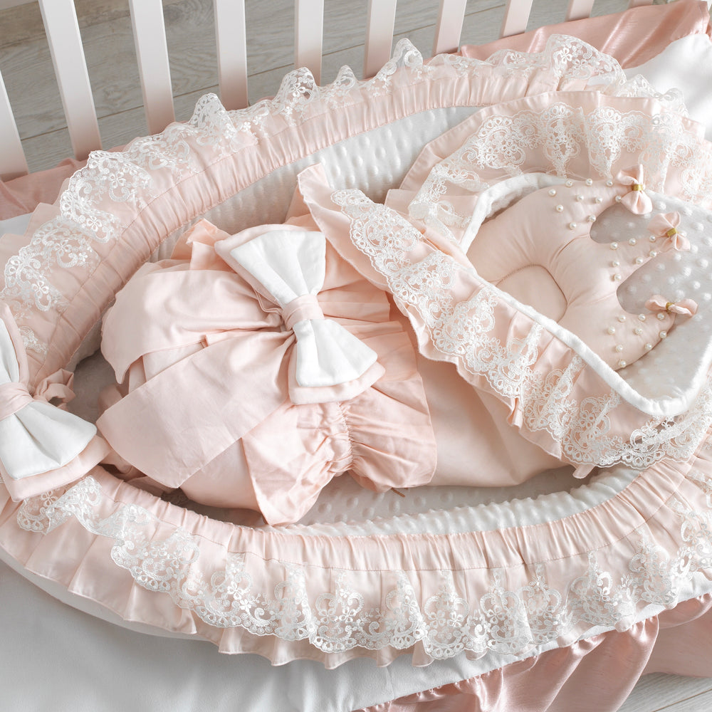 Pink crib bumper with lace details on a white crib