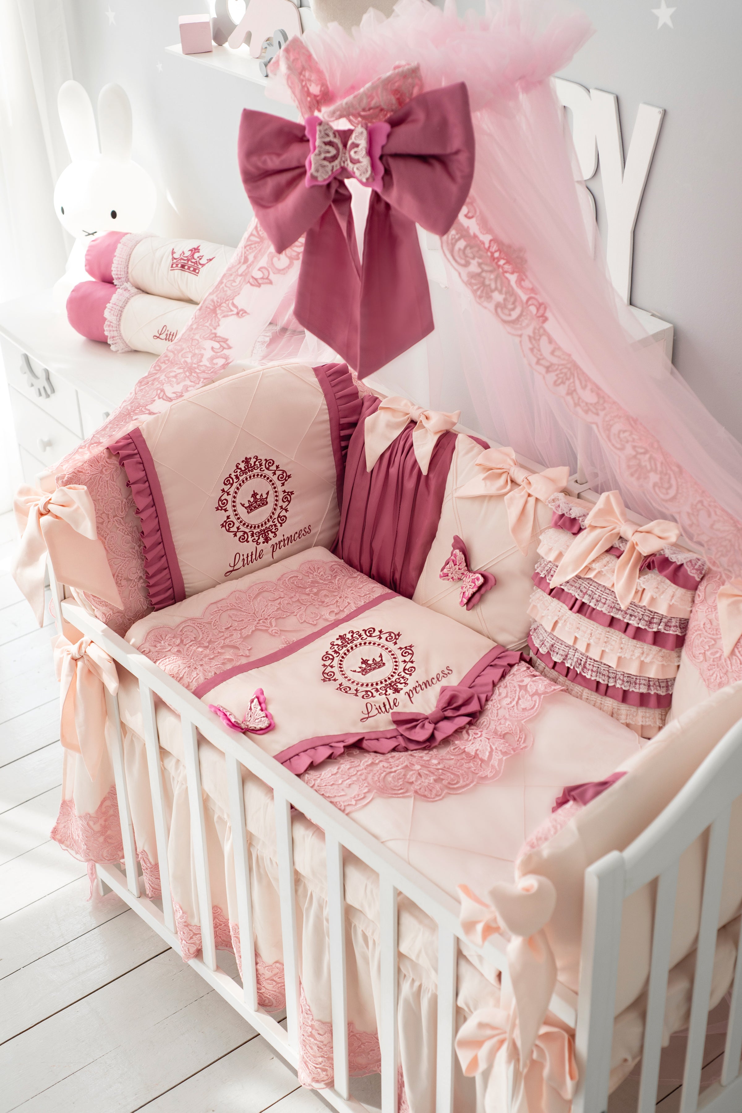 Baby crib bedding set with pink ribbons, lace trim, and matching pillows