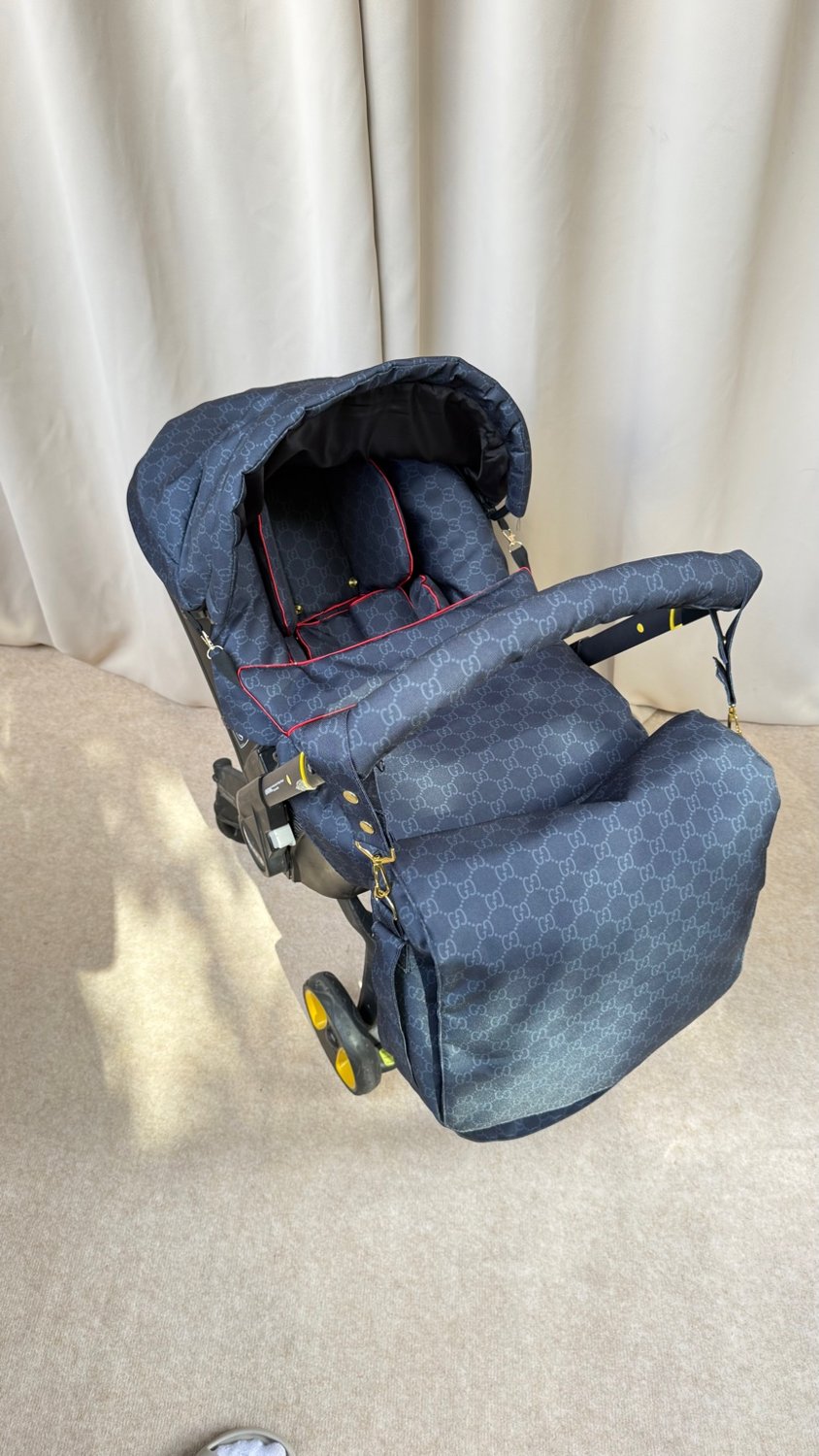 Black monogram Doona+ car seat cover set with red piping and matching padded footmuff, installed on Doona+ stroller frame, front view.