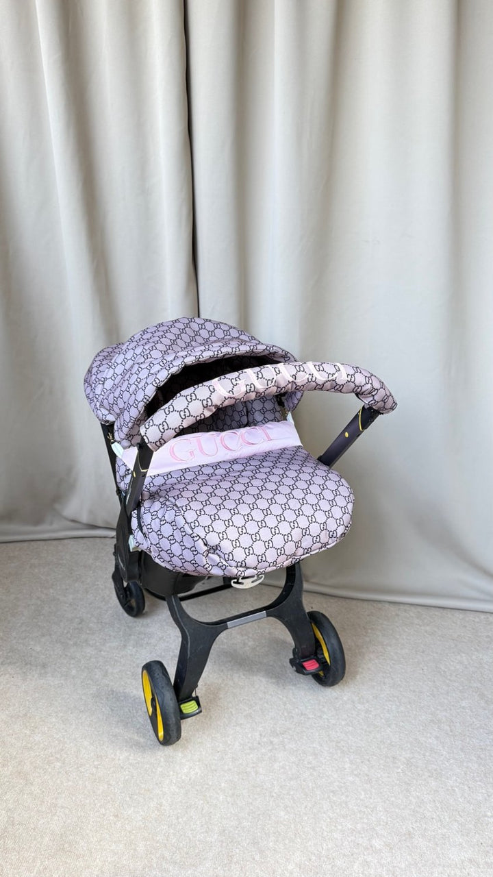 Angled view of beige monogram car seat cover with pink personalized stripe and embroidered pink handlebar cover.