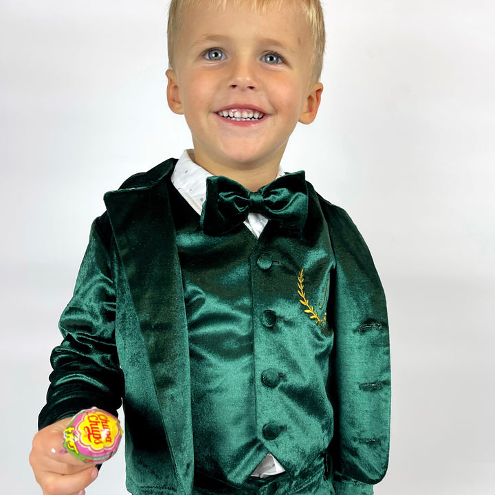 Child wearing a green velvet suit with a bow tie, holding a lollipop against a white background