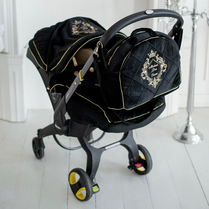 Black velvet Doona car seat cover set with gold piping, embroidered crest and matching quilted diaper bag.