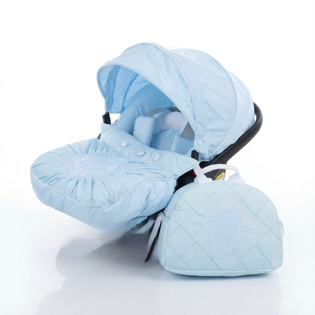 Light blue baby car seat cover set installed on a car seat on a white background, featuring a padded canopy, a quilted footmuff with decorative stitching and white embroidery, and a matching quilted diaper bag with white embroidered detail placed next to the car seat.