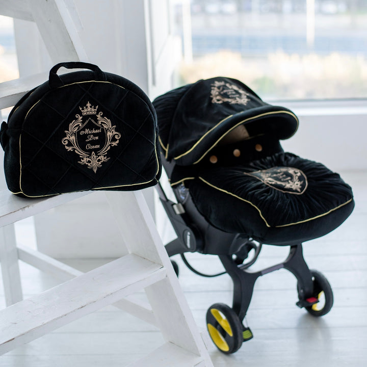 Doona+ black velvet car seat cover set with gold embroidery and matching diaper bag, lifestyle view.