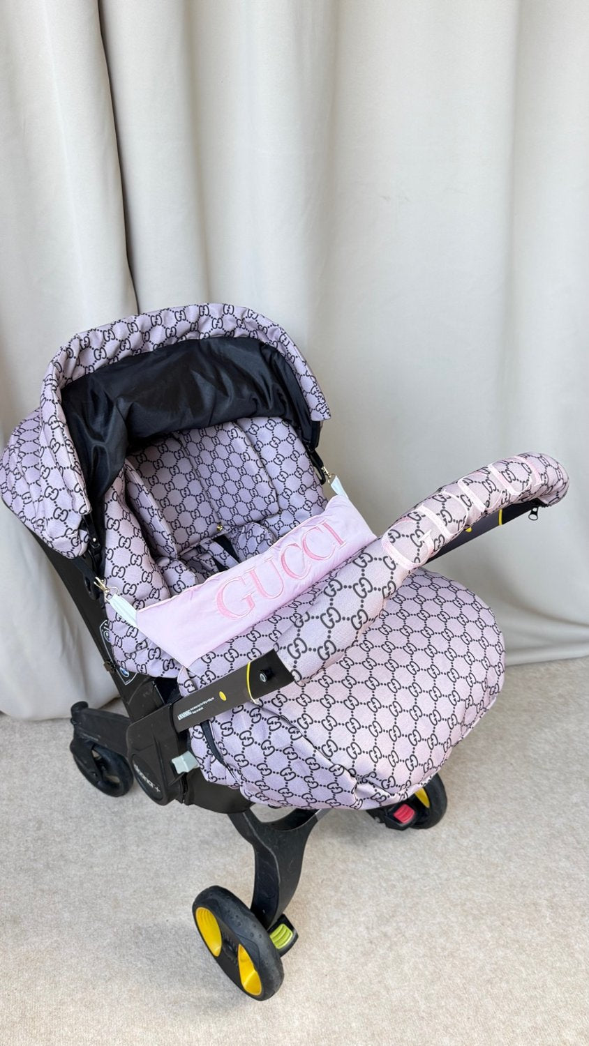 Beige monogram Doona car seat cover set with pink embroidered handlebar cover and personalized pink stripe on footmuff, front view.