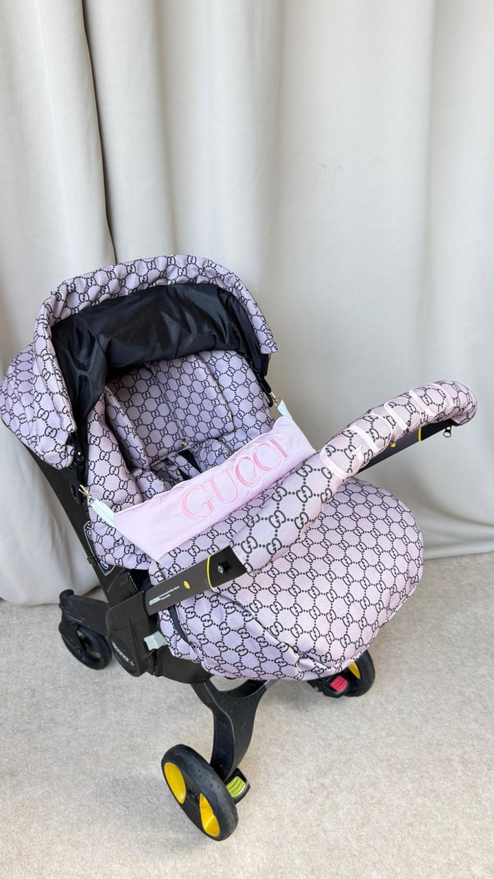 Beige monogram Doona car seat cover set with pink embroidered handlebar cover and personalized pink stripe on footmuff, front view.