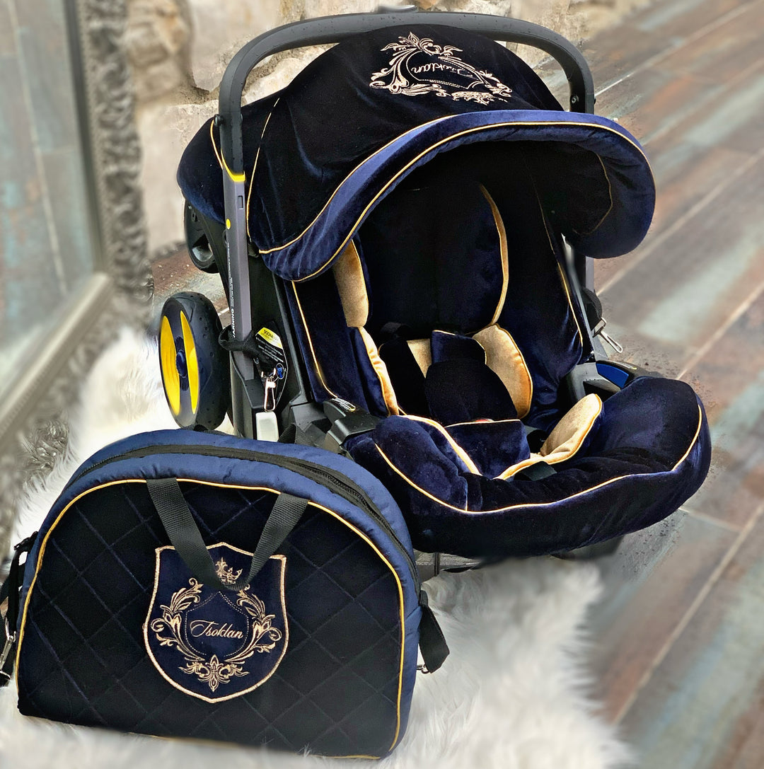 Royal Blue velvet Doona Plus car seat cover set with gold trimming, gold embroidery crest and blue and gold insert, styled on rustic stone wall and rust-tone tile floor.