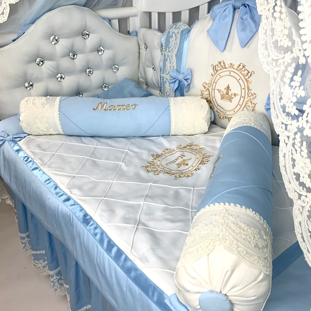 Baby crib with blue and white bedding, decorative pillows, and a name pillow.