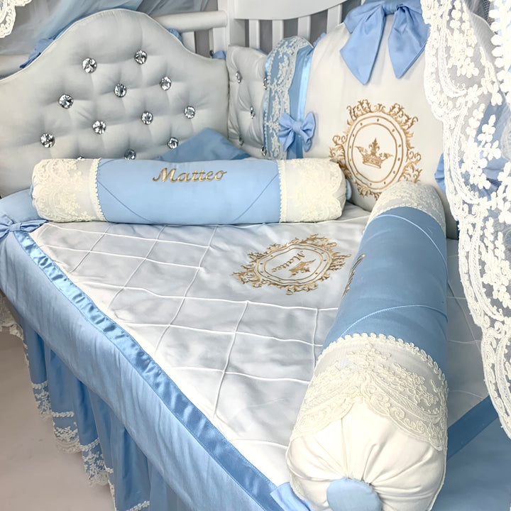 Baby crib with blue and white bedding, decorative pillows, and a name pillow.