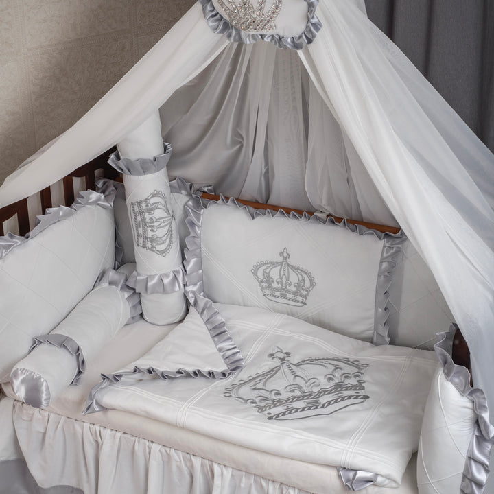 Baby crib with white bedding and gray accents, featuring a crown design.