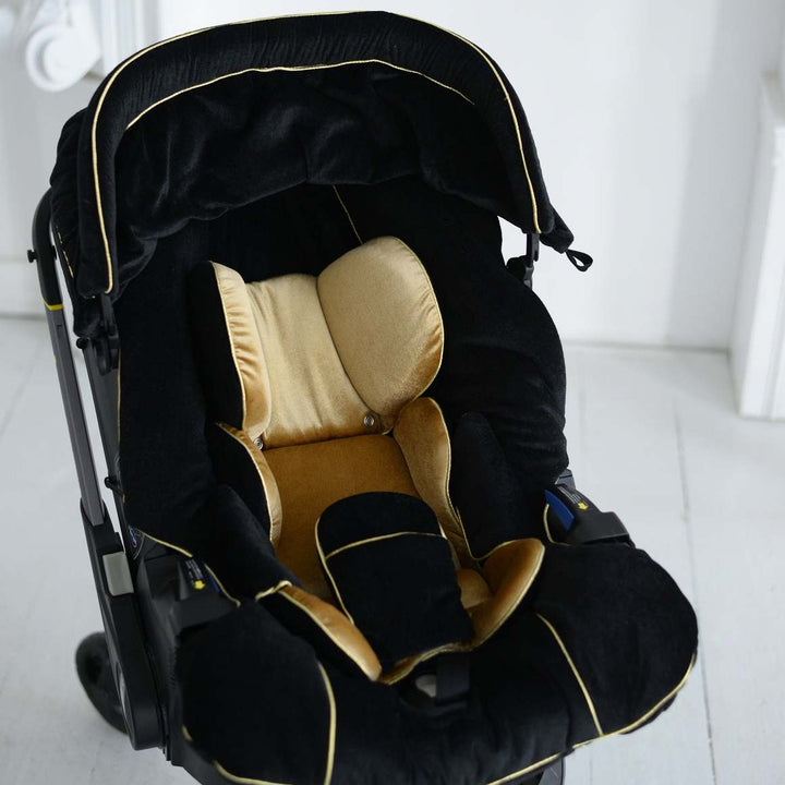 Doona+ black velvet car seat cover close-up with gold infant insert and gold piping.