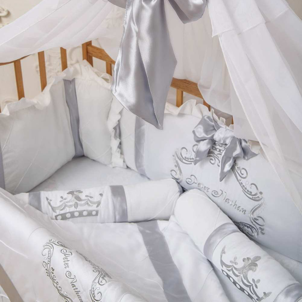 Crib set with white and gray bedding featuring decorative patterns and ribbons.