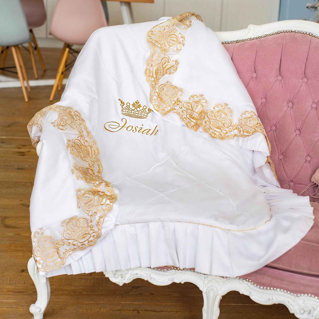 White blanket with gold embroidery and 'Josiah' branding on a pink chair.