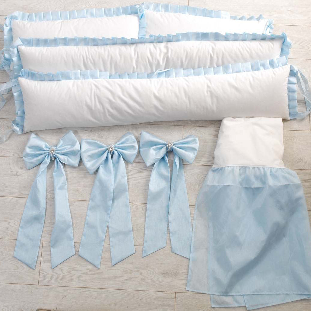 White crib bumper with blue ribbons and skirt on a wooden floor