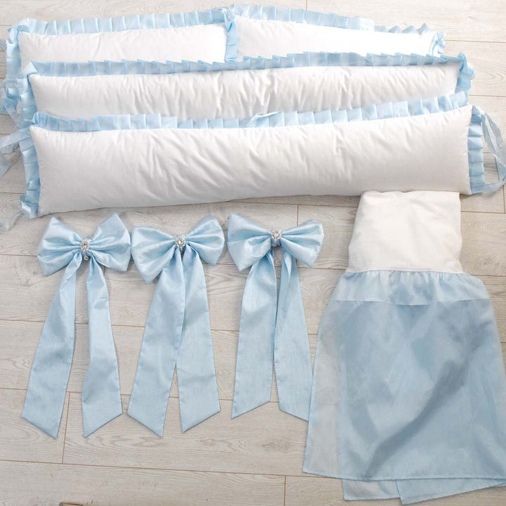 White crib bumper with blue ribbons and skirt on a wooden floor