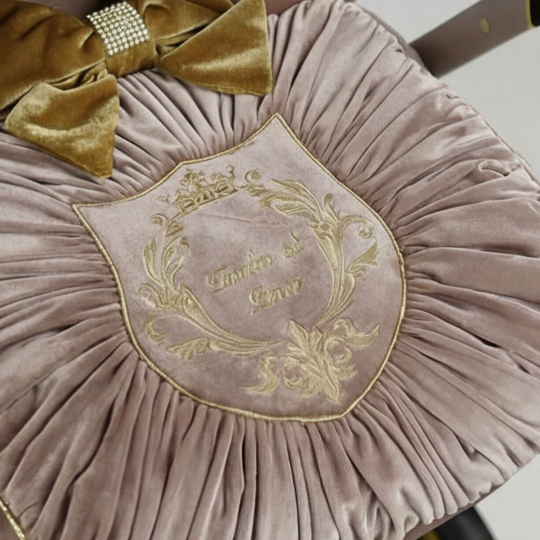 Close-up of dusty rose velvet pleated footmuff with gold embroidered crest and gold velvet bow with rhinestone detail.