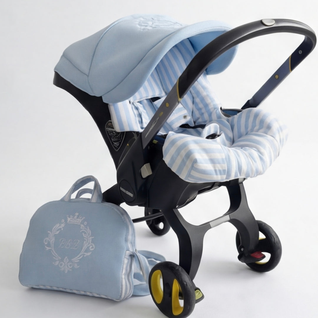 Infant car seat with light blue and white striped fabric seat insert and matching light blue canopy featuring white embroidery, displayed on a black wheeled car seat frame, with a matching light blue diaper bag with white embroidery placed beside it on a light background.