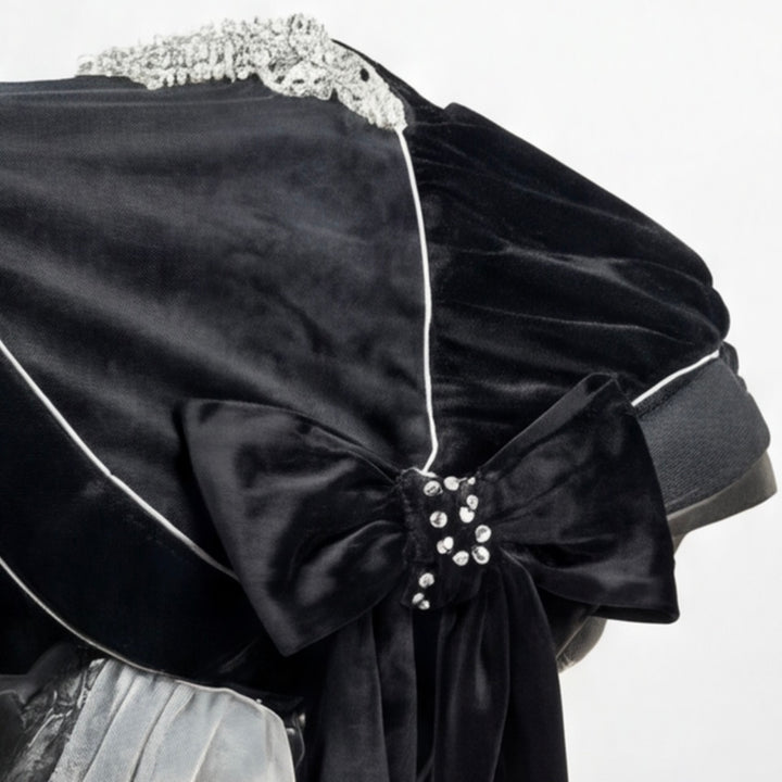 Close-up of a black velour canopy installed on a baby car seat, featuring an elegant oversized bow accented with a rhinestone brooch. The canopy is finished with refined decorative piping, subtle lace detailing along the top edge, and a soft velour fabric with a gentle sheen. The image is photographed on a clean white background.