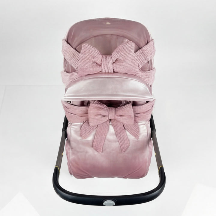 Blush pink velvet Doona+ car seat cover set with shimmering velour finish, ruffled canopy and large bow with long satin ribbons, matching bow on footmuff, installed on Doona+ stroller, side view, white studio background.