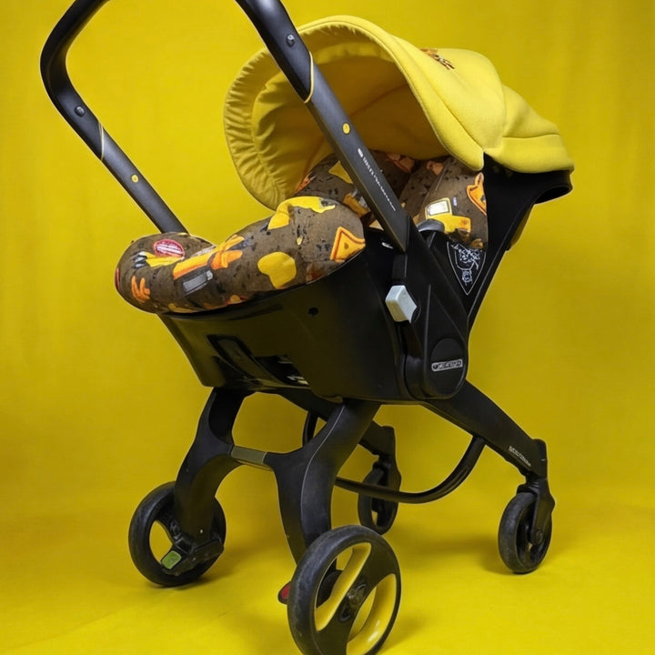 Doona car seat cover set with construction truck print and yellow embroidered canopy.