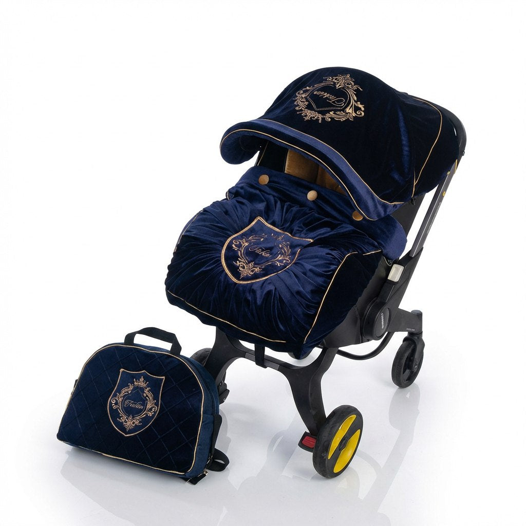 Royal blue velvet infant car seat cover set with gold embroidery, featuring a matching canopy and a rounded-top diaper bag placed beside the car seat, displayed on a wheeled infant car seat frame against a white background.