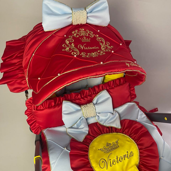 Snow White satin car seat cover set close-up, red and light blue quilted seat cover with yellow center panel, gold personalized embroidery “Victoria,” light blue bow with rhinestone center, red ruffle trim and yellow interior lining, white background.