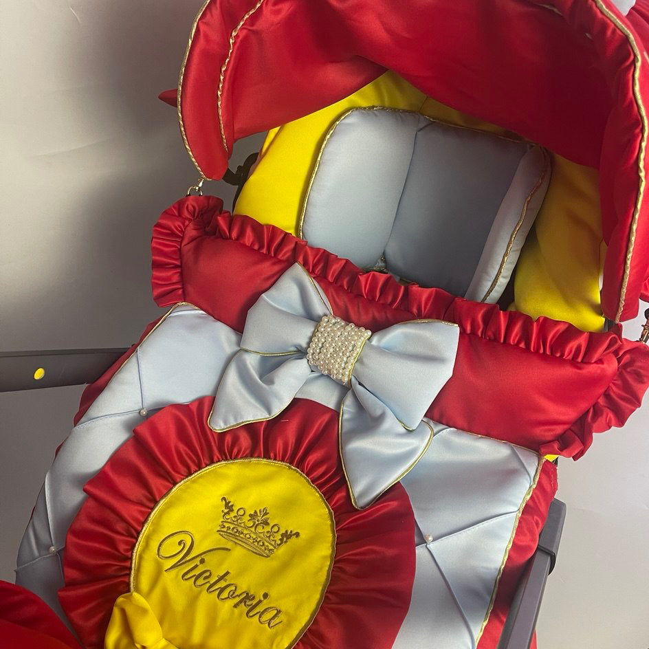 Snow White satin car seat cover set close-up, red and light blue quilted seat cover with yellow center panel, gold personalized embroidery “Victoria,” light blue bow with rhinestone center, red ruffle trim and yellow interior lining, white background.