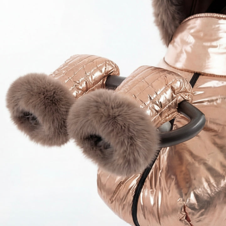 Close-up of rose gold metallic stroller cover mittens with arctic fox fur lining, attached to a stroller handle against a white background.