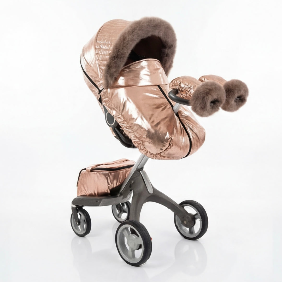 Side view of a rose gold metallic stroller cover set with quilted canopy, arctic fox fur trim, matching footmuff, and mittens, displayed on a stroller frame against a white background.