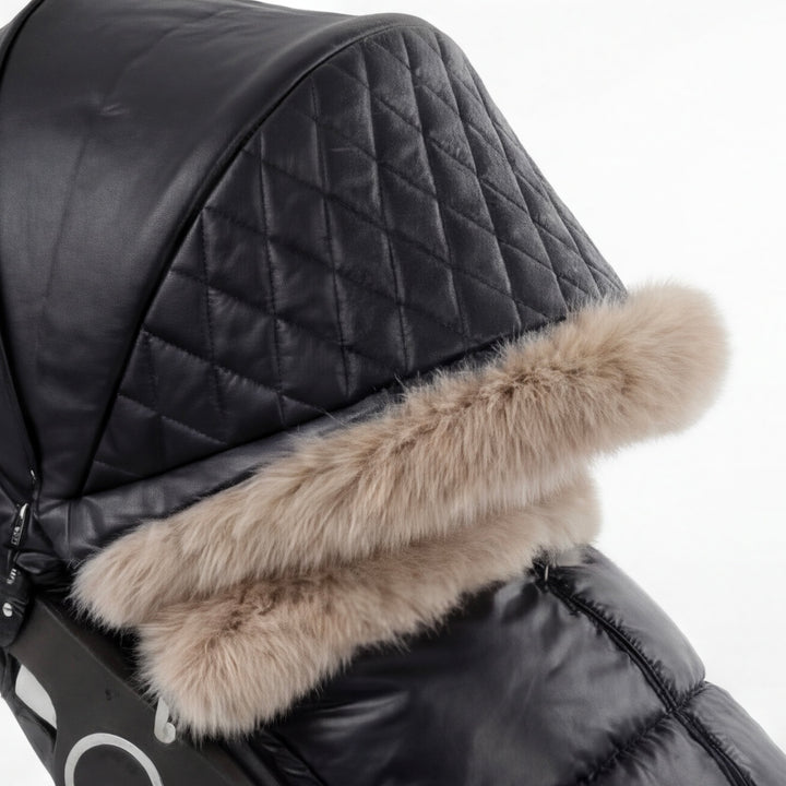 Close-up of a black luxury stroller cover featuring a quilted canopy and beige faux fur trim, shown against a white background.