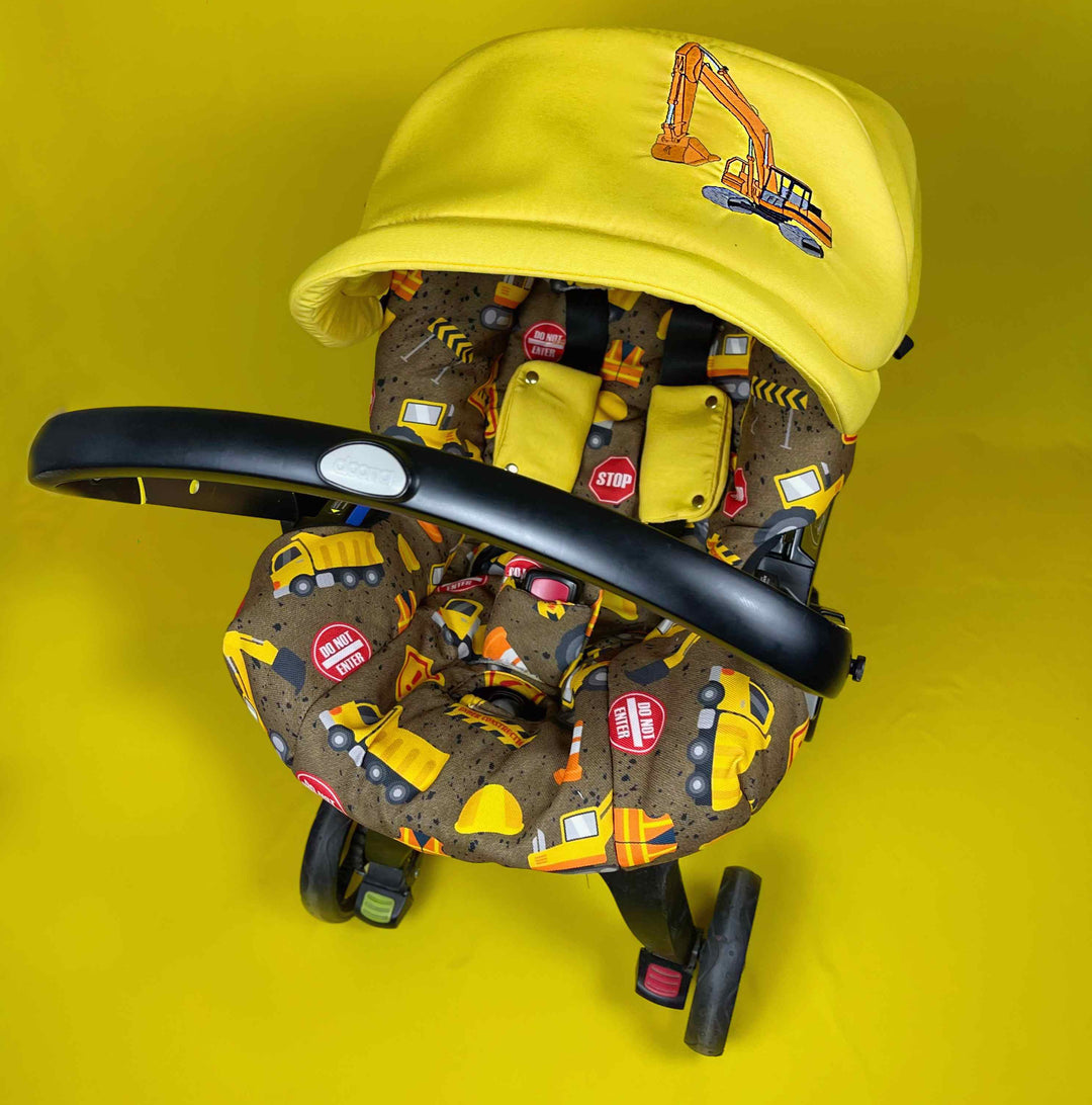 Front view of Doona car seat cover with construction truck print and yellow canopy.