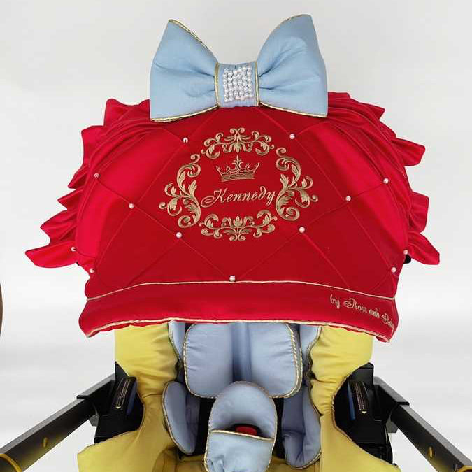 Snow White satin car seat cover set close-up of red quilted canopy with gold personalized embroidery and pearl details, light blue bow with rhinestone center; top view shows yellow interior lining and light blue infant insert on white background.