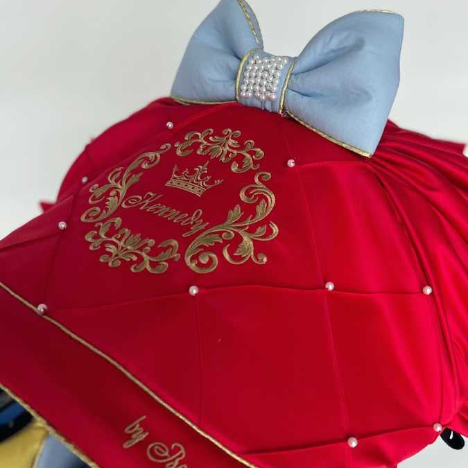 Snow White satin car seat canopy in red with gold embroidery, pearl details and light blue bow with rhinestone center, close-up on white background.