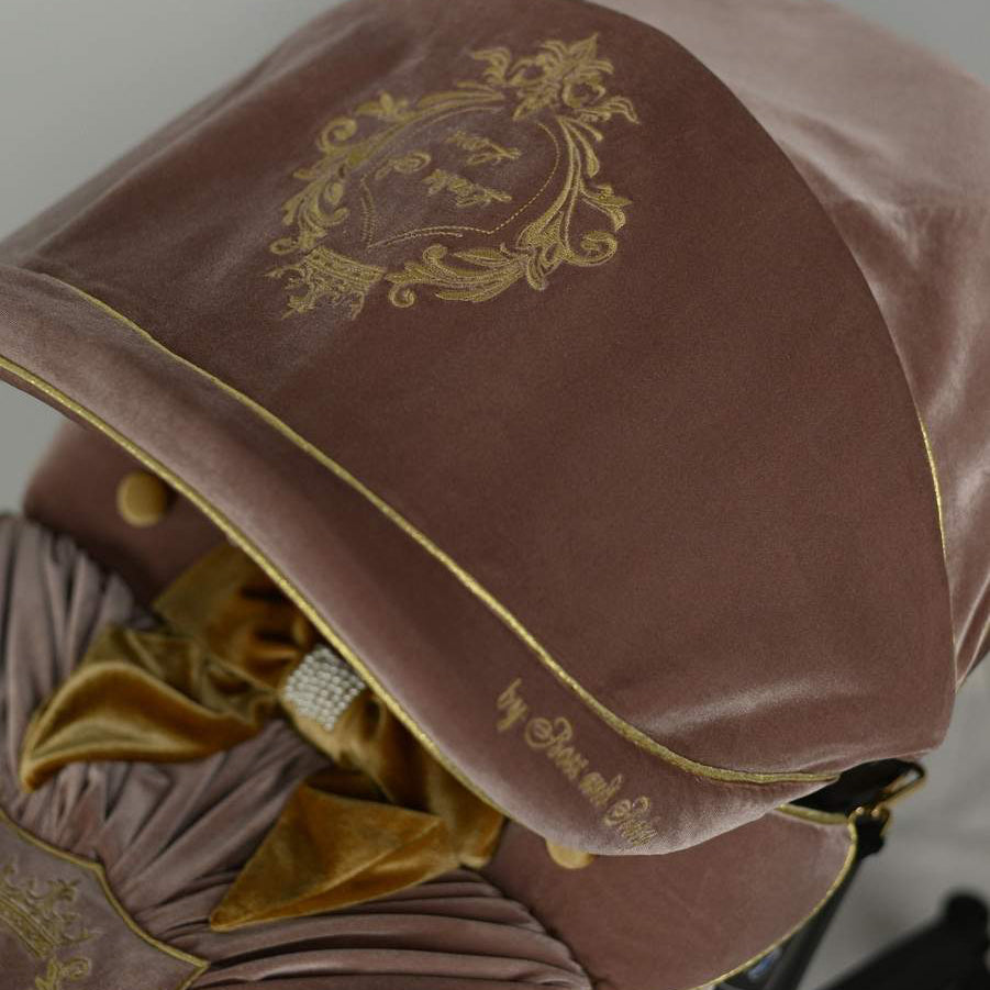 Close-up of dusty rose velvet canopy with gold embroidered crest and gold piping, part of luxury baby car seat cover set.