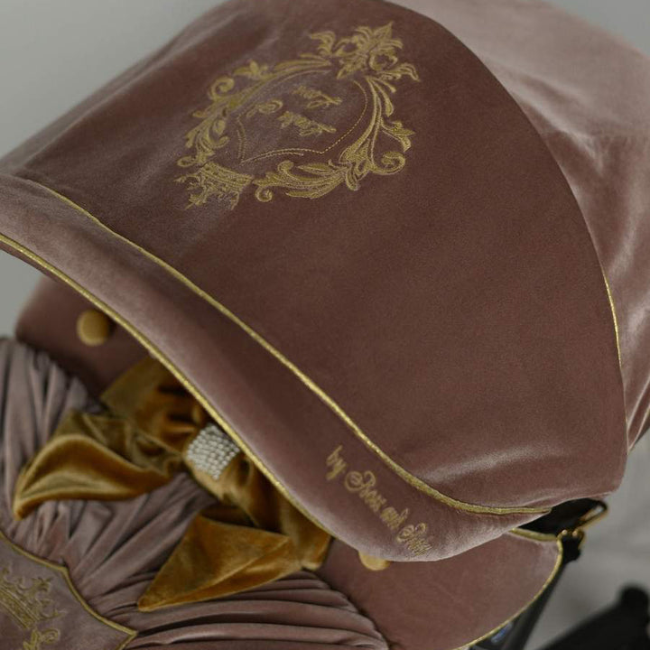 Close-up of dusty rose velvet canopy with gold embroidered crest and gold piping, part of luxury baby car seat cover set.