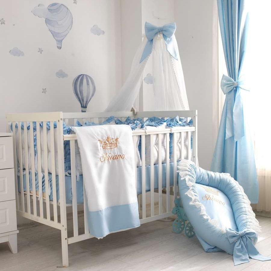 Baby crib with blue and white bedding, canopy, and decorative elements in a nursery.