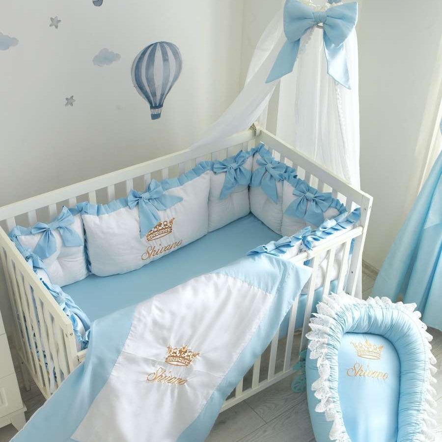 Baby crib with blue and white bedding in a nursery with hot air balloon decor.