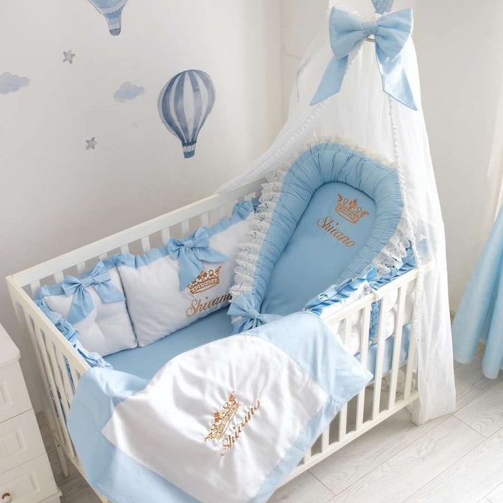 Baby crib with blue and white bedding set featuring a crown design.