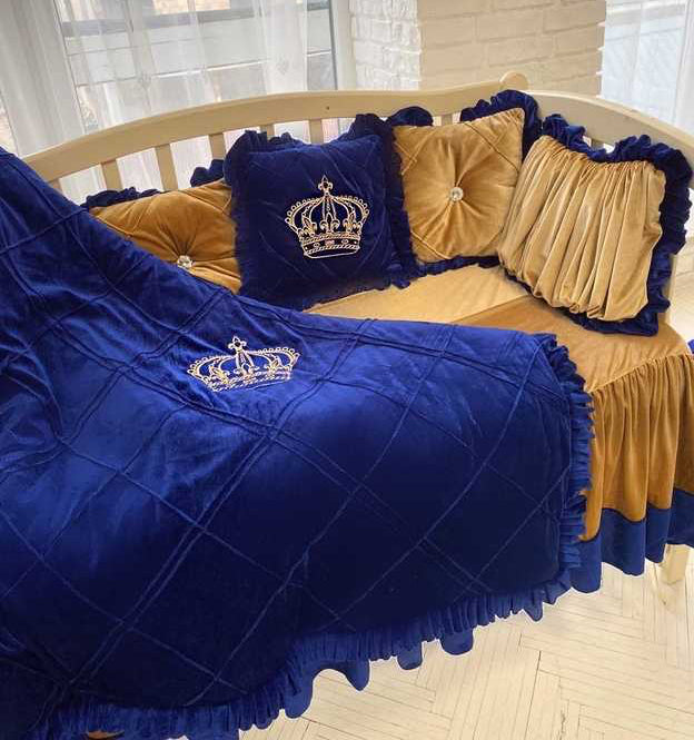 Blue and gold crib set with crown design in a room.
