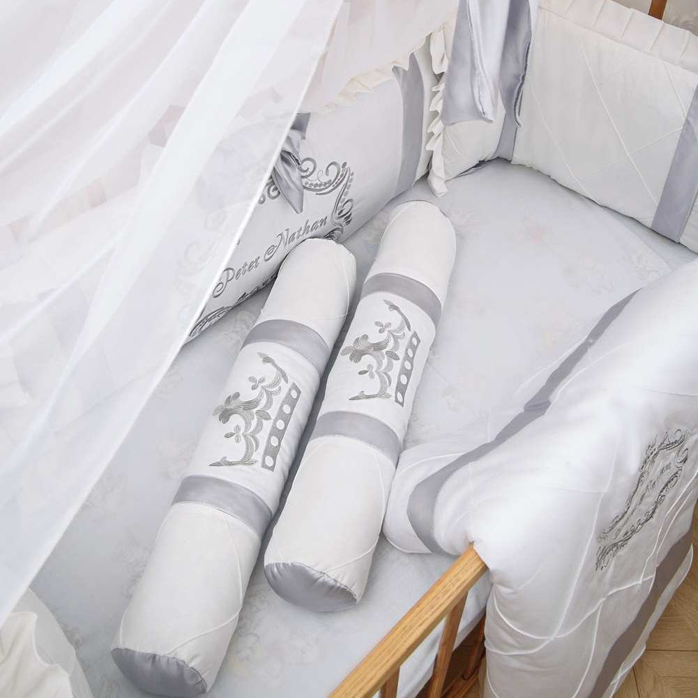 Baby crib with white and gray bedding set, including a bumper and pillows.