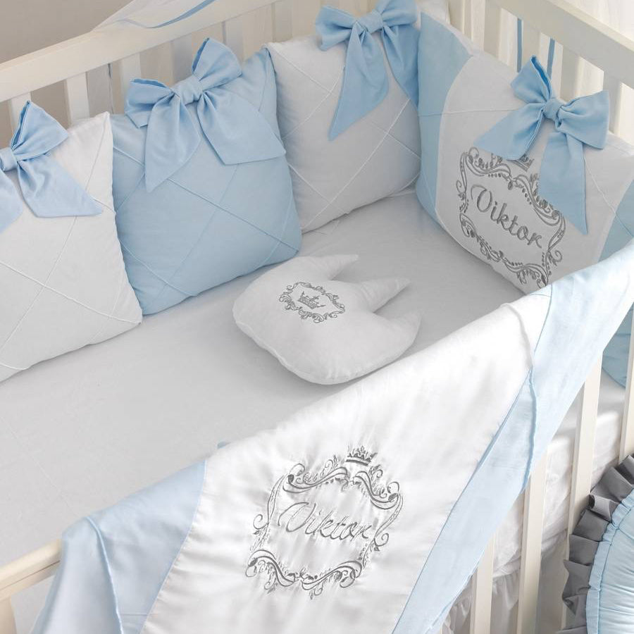 Baby crib with blue and white bedding featuring embroidered names
