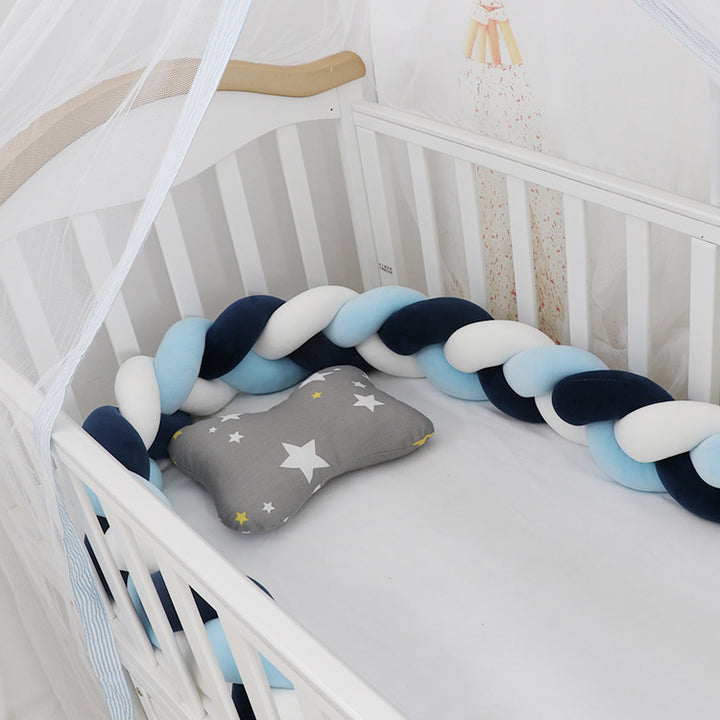 A braided crib bumper set in a crib, featuring a mix of light and dark blue braids with a gray end pillow decorated with a star.
