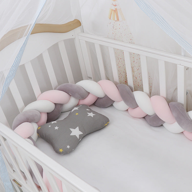 A braided crib bumper set in a crib, featuring a mix of light and dark blue braids with a gray end pillow decorated with a star.