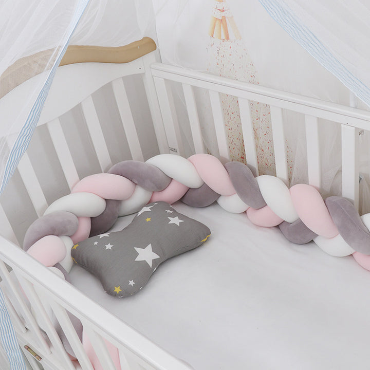 A braided crib bumper set in a crib, featuring a mix of light and dark blue braids with a gray end pillow decorated with a star.