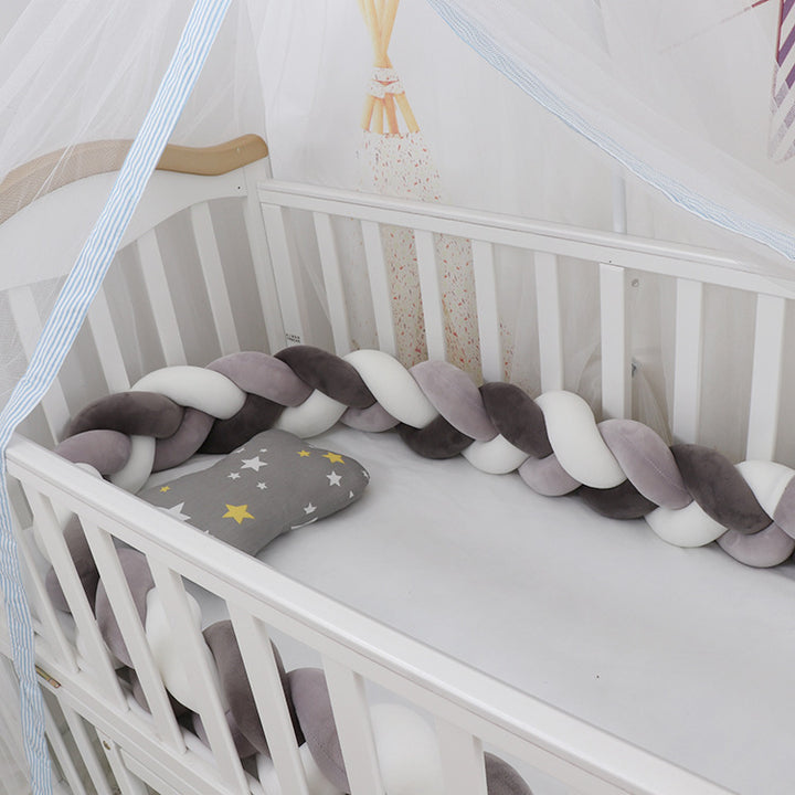 A braided crib bumper set in a crib, featuring a mix of light and dark blue braids with a gray end pillow decorated with a star.